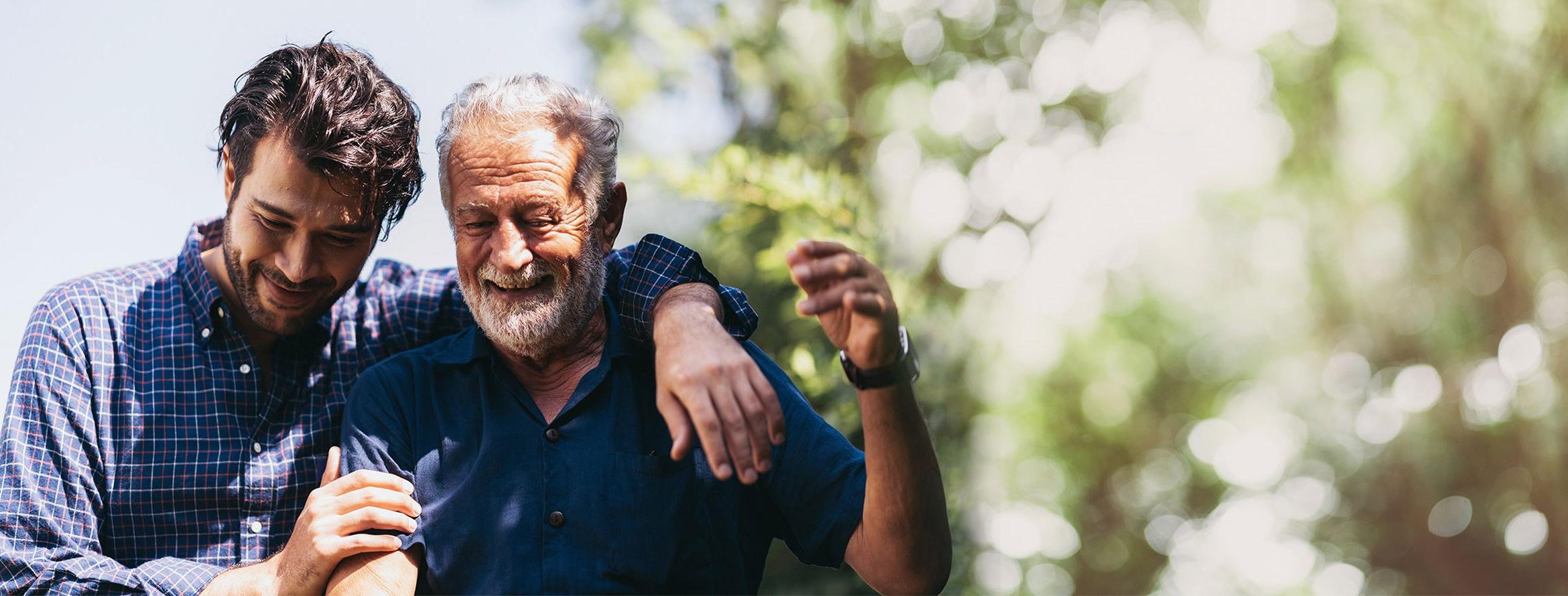 A father and son duo in each other's embrace outside laughing in the sunny weather.